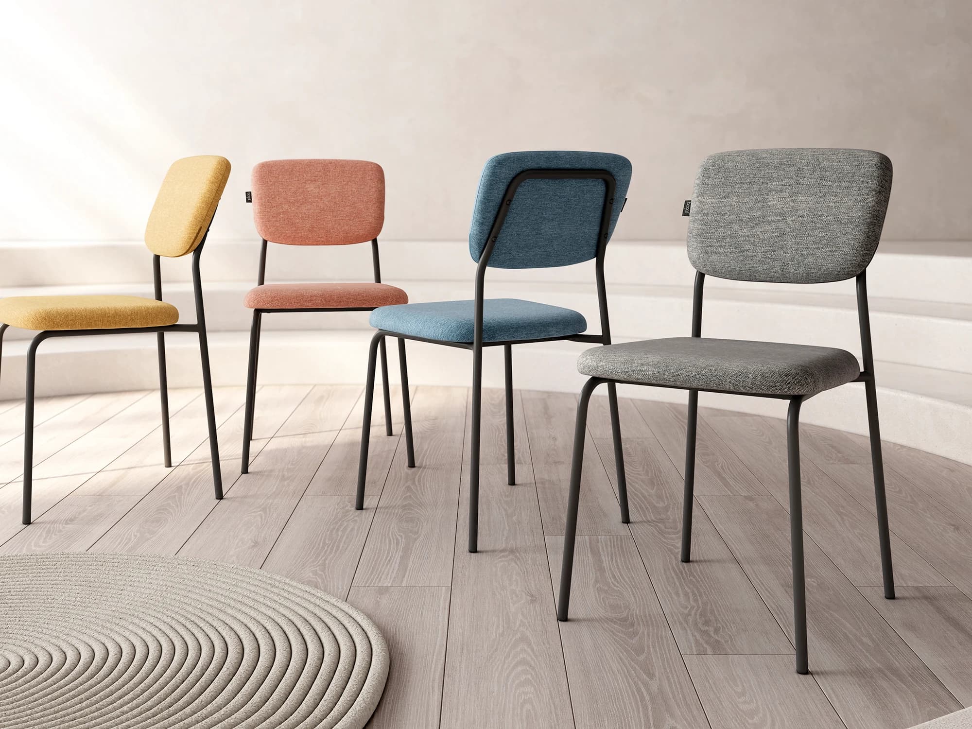 Vier gestoffeerde stoelen in mosterd, terracotta, blauw en grijs op een lichte houten vloer